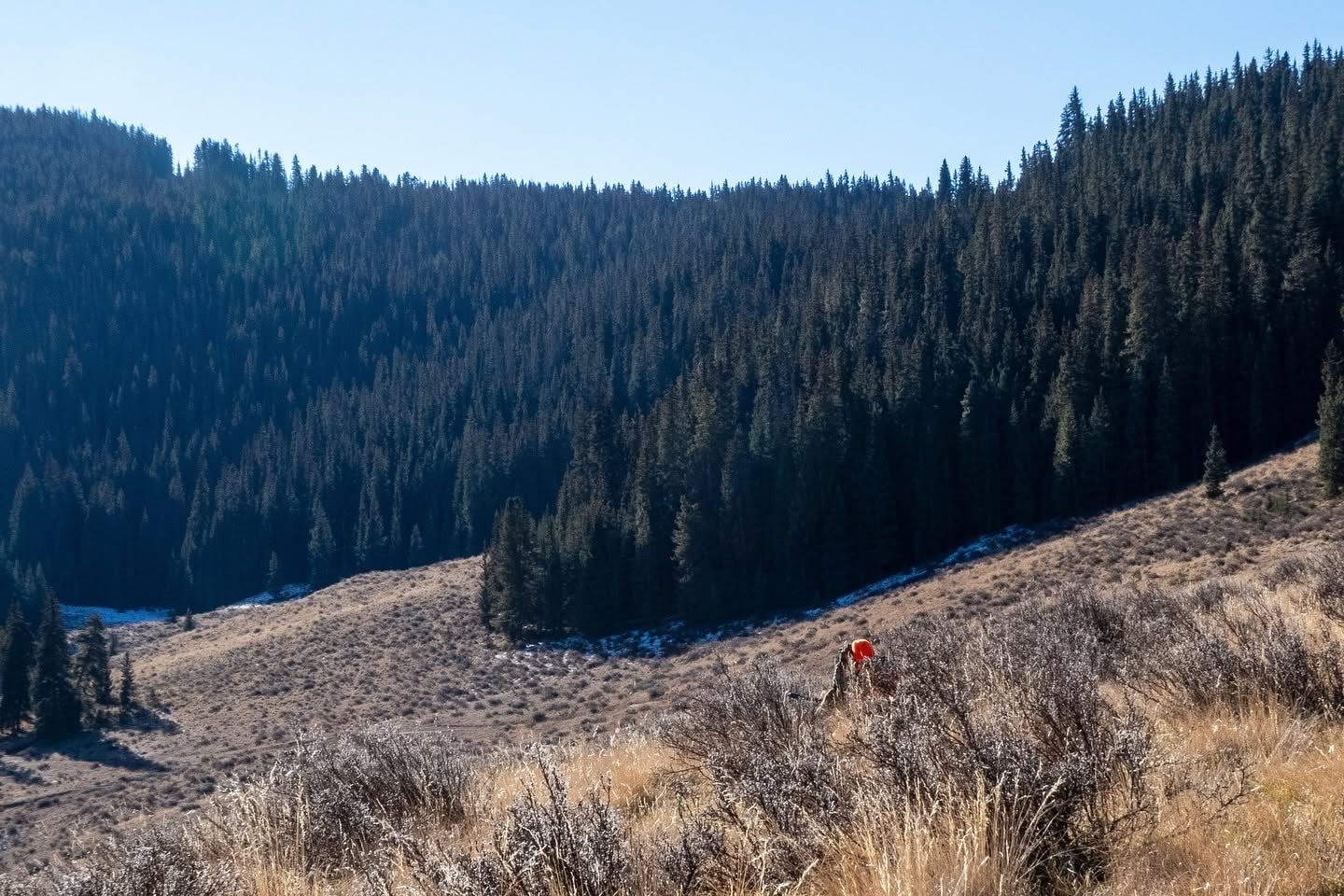 A hunter small against a broad mountain landscape, illustrating the scale of the terrain and the journey