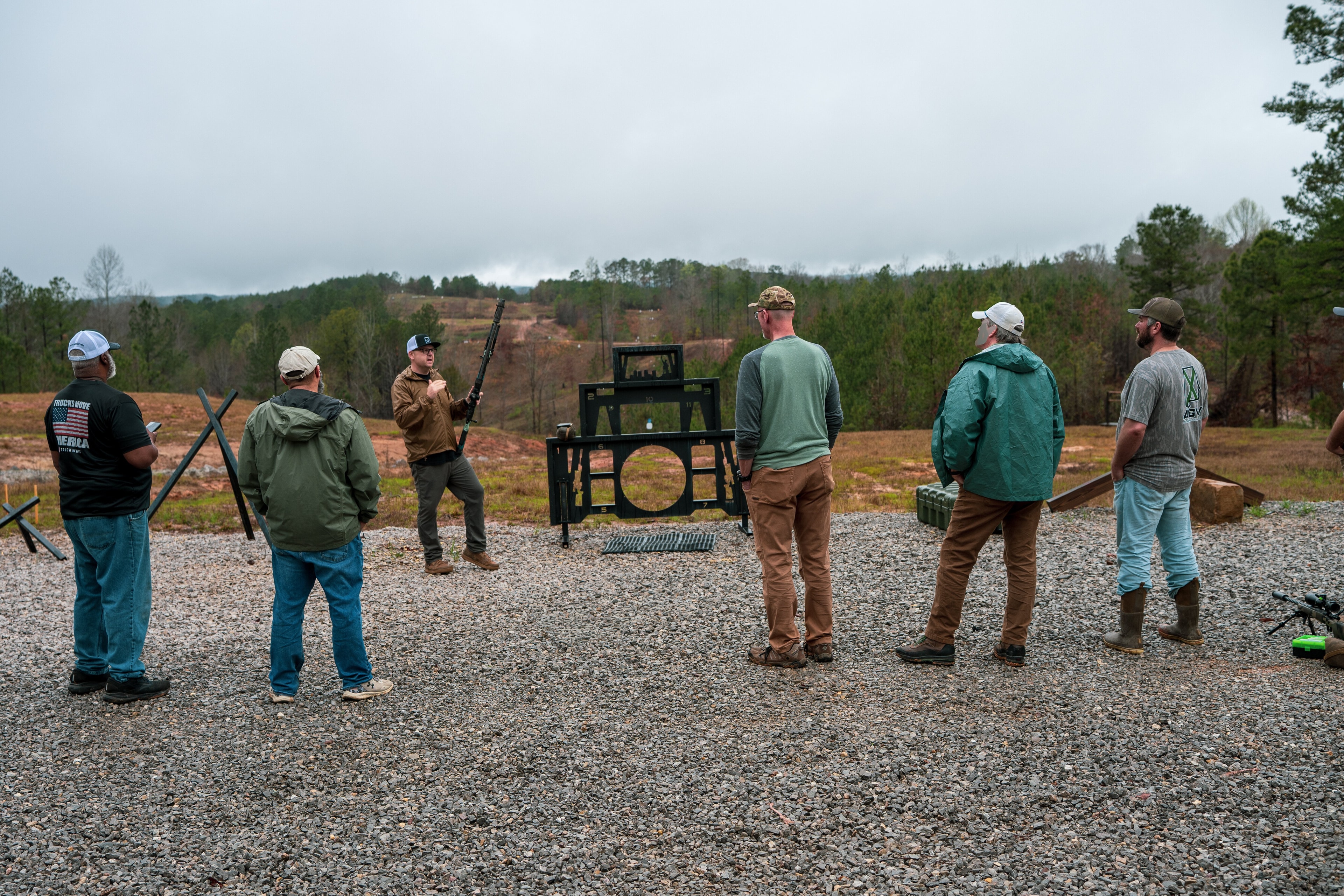 Instructor addressing a group of students at an outdoor shooting range
